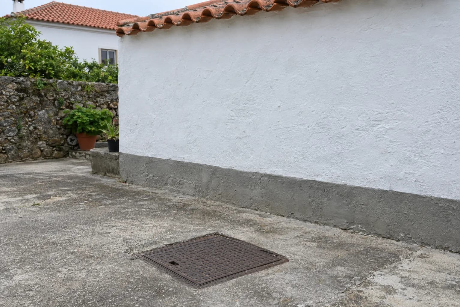 Tampa de ferro de uma caixa de visita no pátio de uma casa caiada